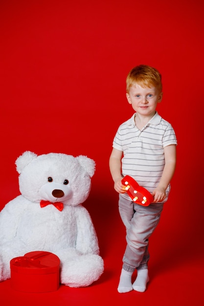 Um menino ruivo de 3 anos segura um coração vermelho nas mãos para o Dia dos Namorados