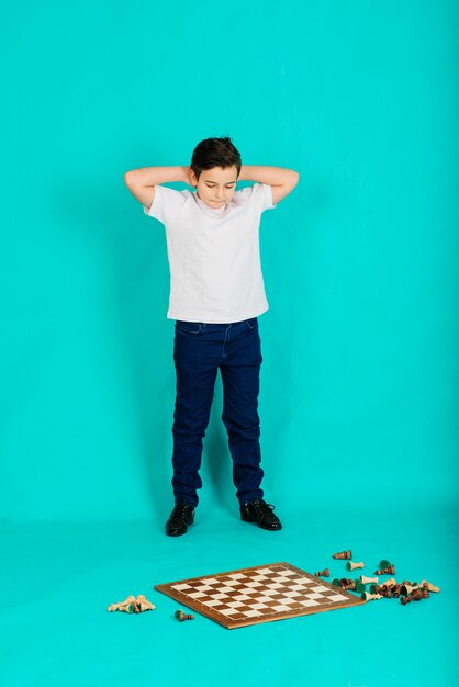 Um menino segura um tabuleiro de xadrez nas mãos e olha para ele, fazendo uma pose emocionada