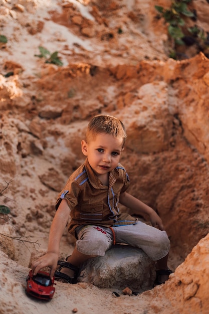 Um menino senta-se na areia brincando com um pequeno carro