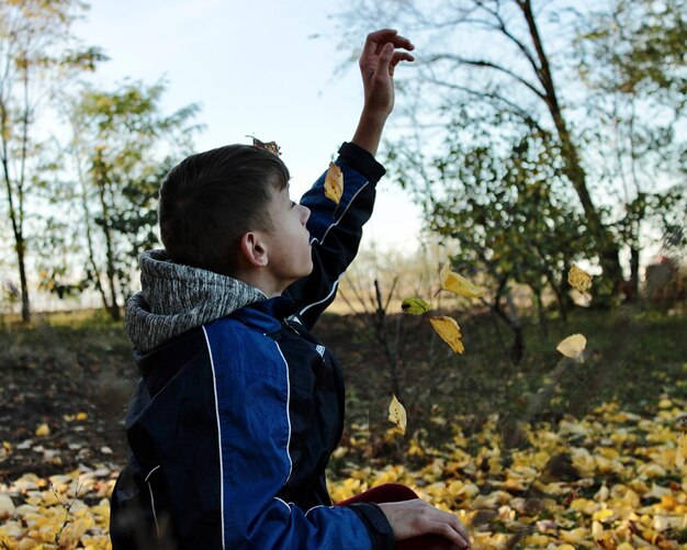 Foto um menino sentado sob uma árvore no jardim pega folhas de outono que caem