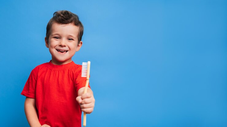 Foto um menino sorridente com dentes saudáveis segura uma escova de dentes em um fundo azul isolado higiene oral um lugar para o seu texto