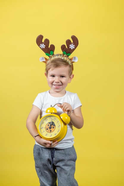 Um menino sorridente em fantasia de rena de natal com despertador