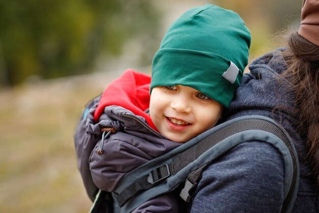 Um menino sorridente viaja atrás de sua mãe em um portador de bebê