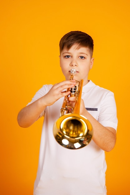 Um menino toca trompete. Um adolescente bonito com uma camiseta branca toca um instrumento musical de trompete