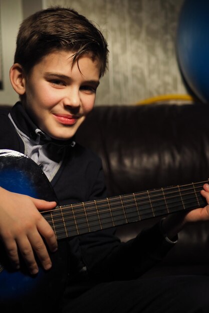 Um menino tocando violão em uma sala com uma bola azul ao fundo.