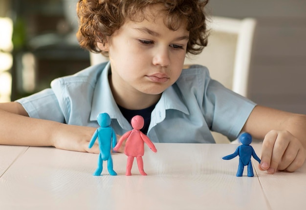 Um menino triste brinca com figuras de plasticina de uma família onde pais e filhos são separados