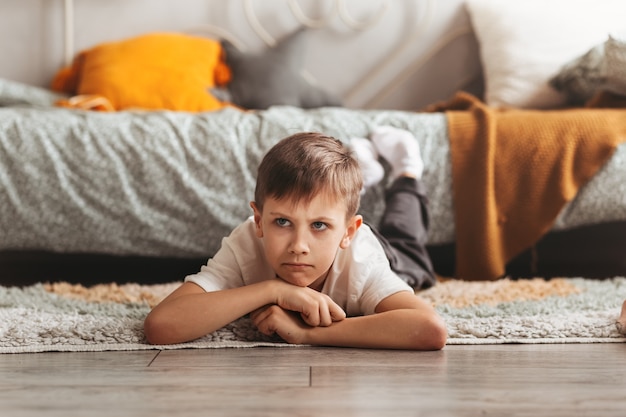 Um menino triste está deitado no chão do quarto das crianças. Emoções infantis. Adolescente zangado