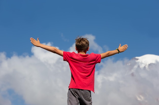 Um menino turista está no topo de uma colina com os braços estendidos para os lados contra o azul
