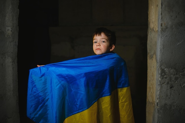 Foto um menino ucraniano triste envolto em uma bandeira ucraniana se escondendo de bombardeios em um abrigo antiaéreo na cidade de mariupol ou kiev a agressão da rússia a guerra na ucrânia e 2022