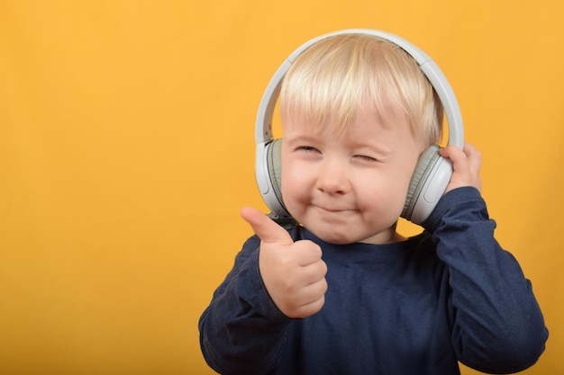 Um menino usando fones de ouvido com um polegar para cima em um fundo amarelo