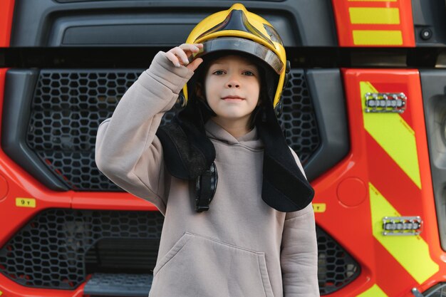 Foto um menino usando um capacete firemans perto de um caminhão de bombeiros