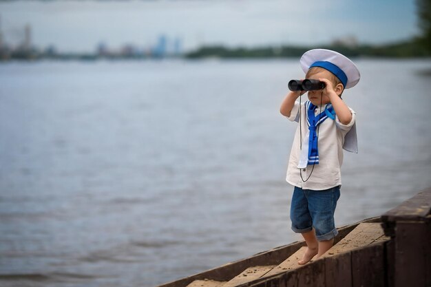 Um menino vestido de marinheiro fica na praia e olha através de binóculos