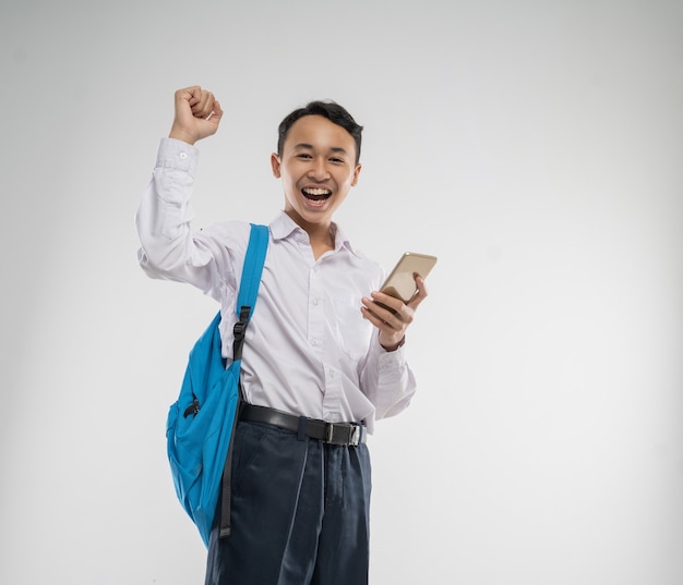 Um menino vestindo um uniforme do ensino fundamental sorriu feliz enquanto segurava um celular com a mão levantada