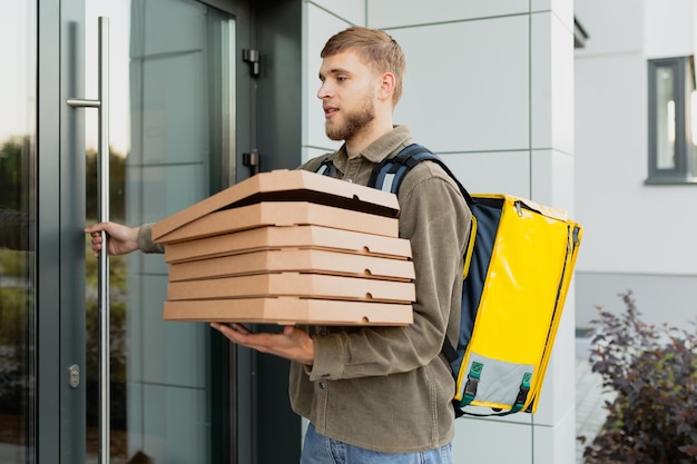 Um mensageiro com caixas de pizza entra na entrada de um prédio residencial para entregar um pedido Entrega profissional em uma cidade grande