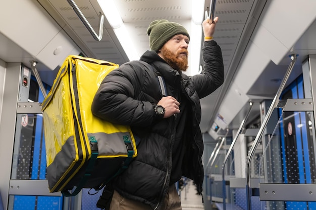 Um mensageiro masculino com uma mochila amarela anda no metrô Entrega de pizza a um cliente em uma megalópole