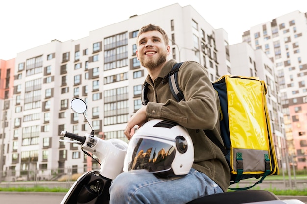 Foto um mensageiro sorridente em uma scooter com uma bolsa amarela o entregador estacionou perto da casa para entregar pizza ao cliente