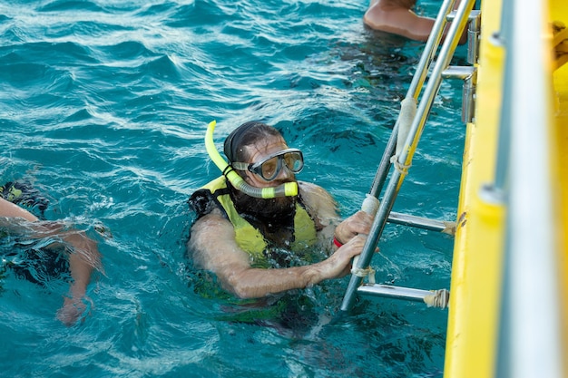 Um mergulhador barbudo em um colete salva-vidas sobe a bordo de um barco no mar