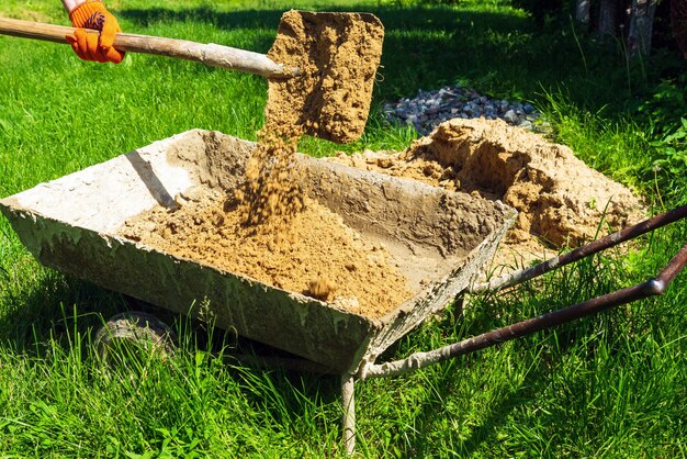 Um mestre construtor despeja areia em um carrinho com uma pá para fazer concreto