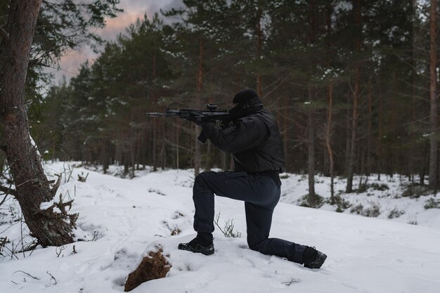 Foto um militar com um rifle de assalto moderno mira enquanto está sentado de joelho na floresta de inverno