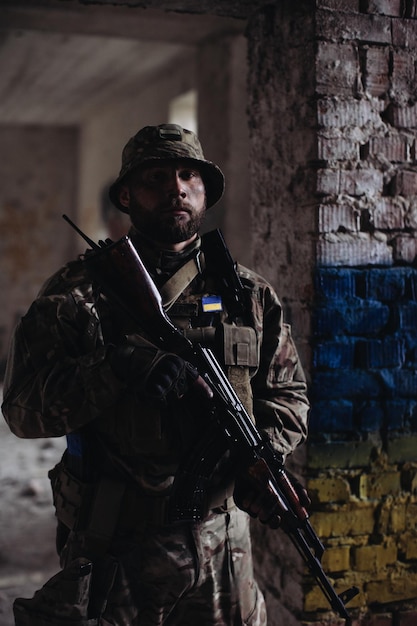 Um militar ucraniano com uma arma nas mãos fica no contexto da bandeira da Ucrânia A bandeira da Ucrânia é pintada em uma parede de tijolos