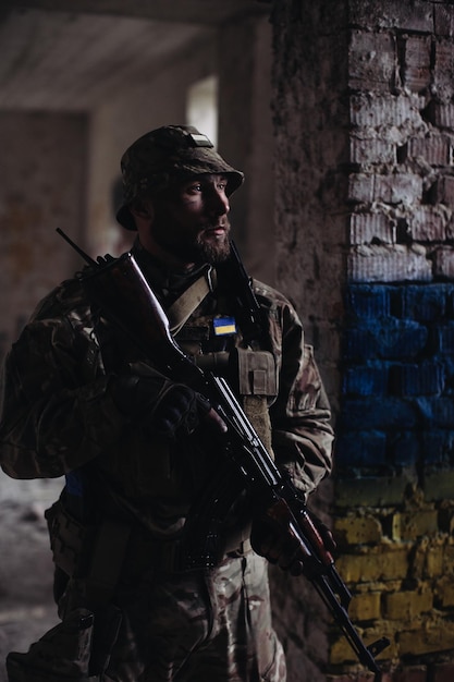 Um militar ucraniano com uma arma nas mãos fica no contexto da bandeira da Ucrânia A bandeira da Ucrânia é pintada em uma parede de tijolos