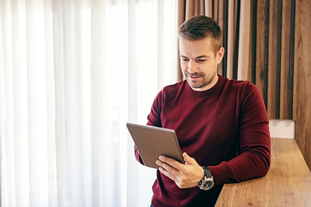 Um millennial contemporâneo está rolando no tablet enquanto está em casa