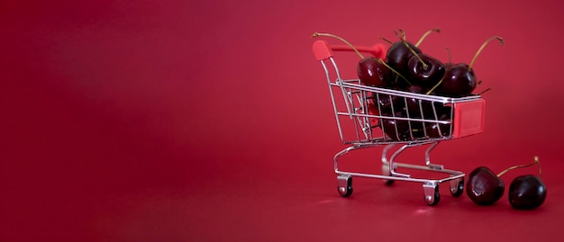 Um mini carrinho de supermercado de metal cheio de suculentas cerejas vermelhas em um espaço de cópia de fundo bárdico