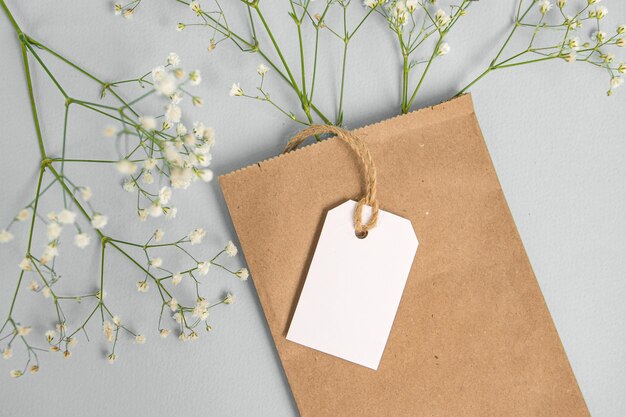 Foto um modelo de um rótulo branco e uma etiqueta de preço perto de um saco de artesanato com flores sobre uma mesa cinzenta