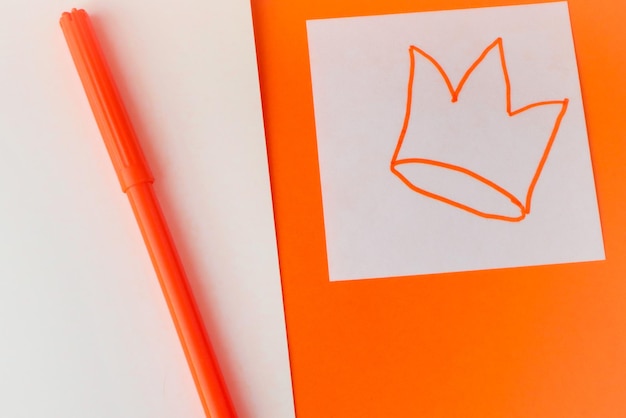 Um modelo nas cores tradicionais da celebração do Dia do Rei na Holanda Fundo laranja e branco em meia vista superior com uma coroa fofa desenhada à mão com uma caneta de feltro laranja