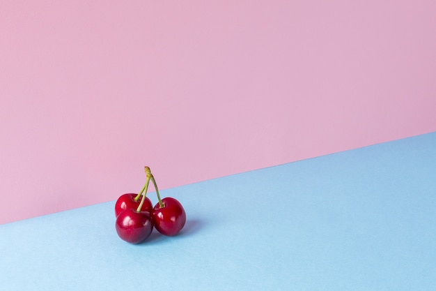 Um monte de cerejas sobre um fundo azul e rosa claro