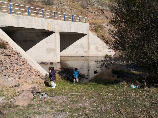 Foto um monte de crianças a brincar ao lado do rio contra a ponte.
