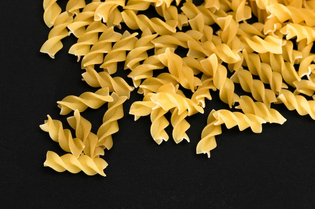 Um monte de macarrão fusilli cru espalhado na mesa preta