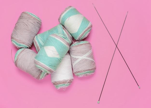 Foto um monte de novelos de fios de lã de cores pastel, agulhas de tricô no fundo rosa do estúdio. vista do topo. tiro do estúdio. hobby homebrew