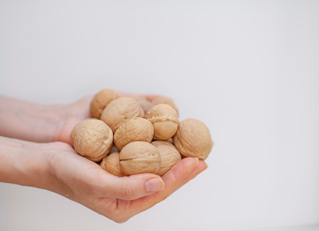 Um monte de nozes inteiras nas mãos de mulheres em um close-up de fundo branco. Alimentos saudáveis e orgânicos com alto teor de proteínas e proteínas.