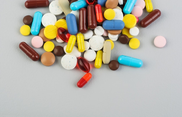 Um monte de pílulas e cápsulas de cores diferentes em uma superfície cinza