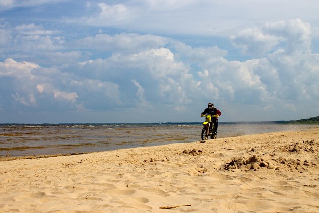 Foto um motociclista anda ao longo de uma praia de areia com o lago peipsi no fundo na região de pskov, na rússia