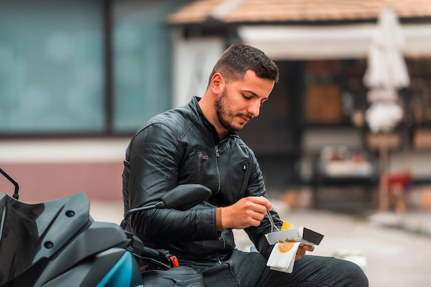 Um motociclista moderno encostado em uma motocicleta come doce em uma pausa do trabalho Foco seletivo