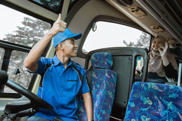 Um motorista do sexo masculino em um uniforme azul fez aos passageiros um sinal de positivo com o polegar como um sinal para o ônibus sair enquanto estava sentado no ônibus