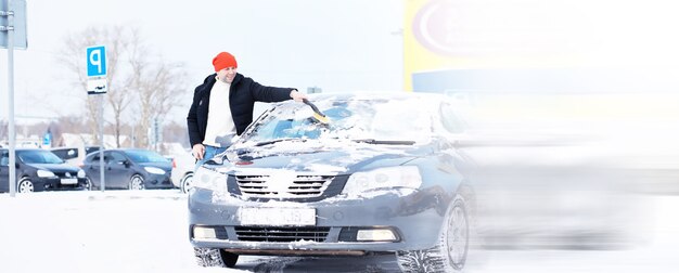Um motorista do sexo masculino está parado na frente de um carro. o proprietário limpa o carro da neve no inverno. carro depois de uma nevasca.