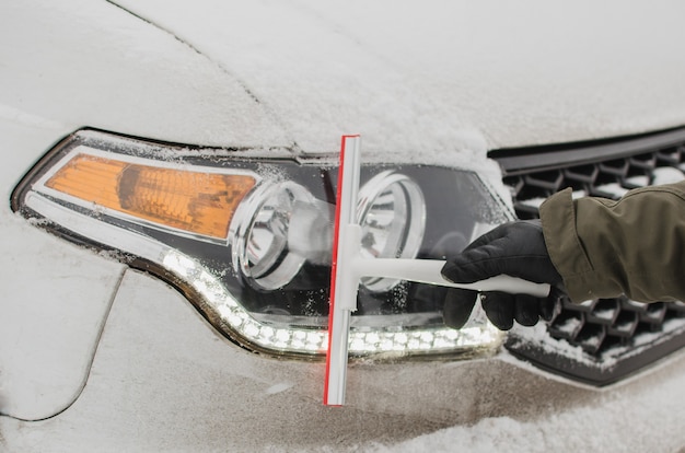 Um motorista limpando os faróis de um carro da neve no inverno.