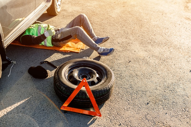 Um motorista ou trabalhador repara um carro quebrado na berma da estrada. Vista de cima. O homem está debaixo do carro