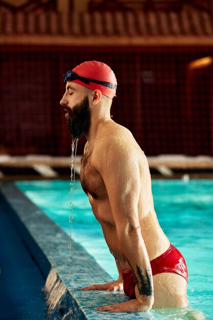 Um nadador de chapéu e óculos ao lado da piscina um nadador masculino emerge da piscina em um vermelho