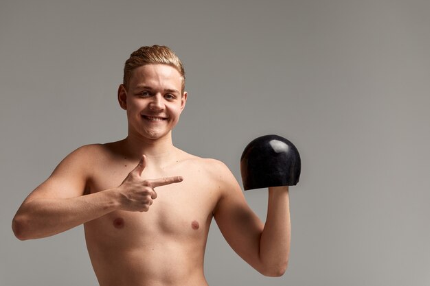 Um nadador, um jovem atleta em excelente forma física, mostra com a mão instando para começar os treinos, um banner publicitário, um fundo cinza, uma cópia do espaço.