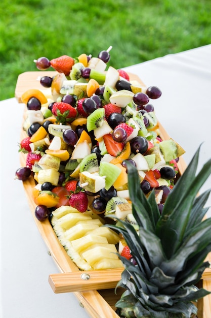 Um navio de madeira decorado com frutas frescas em um espeto fica em uma mesa festivaFoto vertical