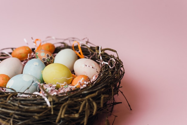 Um ninho de galhos e feno e um enchimento de papel rosa com ovos de Páscoa de cor pastel. Ovos pintados e decorativos para um feriado de Páscoa leve. Cartão de Páscoa em um fundo rosa