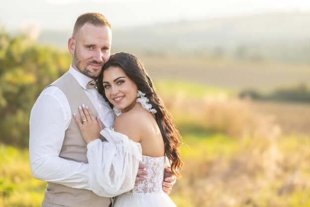 Foto um noivo elegante de terno bege e uma linda noiva morena de vestido branco estão se abraçando ternamente