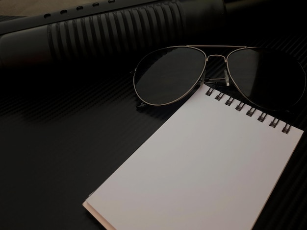 Um notebook e óculos de sol estão em uma superfície preta.