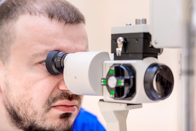 Foto um oftalmologista masculino verifica a visão de um paciente com um dispositivo moderno com um feixe de luz