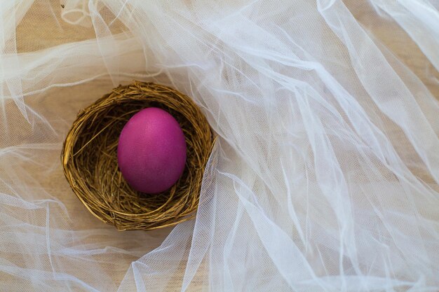 Um ovo roxo de Páscoa está em um ninho em um véu branco Decoração de Páscoa Decoração de Páscoa de primavera