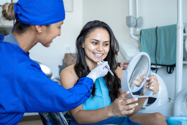 Foto um paciente sorri e se olha no espelho enquanto é visto pelo dentista